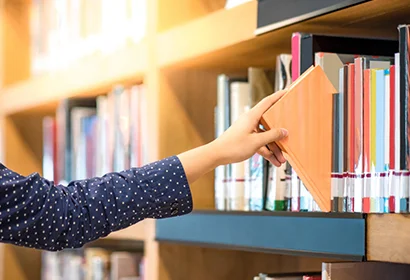 Woman reaching for a book on a shelf.